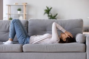Full length young woman lying on couch suffers from anxiety attack